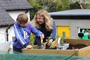 Woman with seedling smiles at boy holding trowel