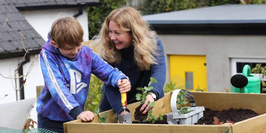 Woman with seedling smiles at boy holding trowel